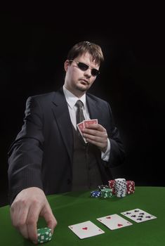 Man in suit with sun glasses playing poker on green table. Chips and cards on the table.