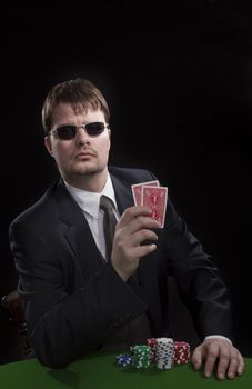 Man in suit with sun glasses playing poker on green table. Chips and cards on the table.