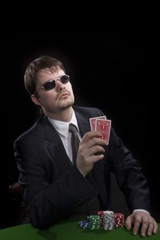 Man in suit with sun glasses playing poker on green table. Chips and cards on the table.