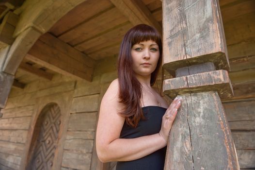 Young beautiful woman leans on arch of homestead.
