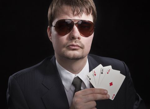 Man in suit with sun glasses playing poker on green table. Chips and cards on the table.