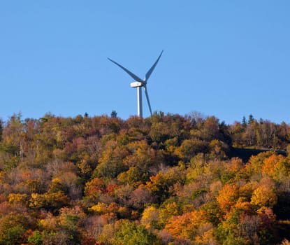 Large wind generator on hilltop above autumn trees