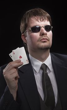 Man in suit with sun glasses playing poker on green table. Chips and cards on the table.