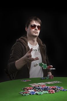 Man with sun glasses playing poker on green table. Chips and cards on the table.