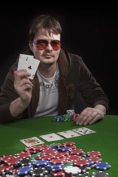 Man with sun glasses playing poker on green table. Chips and cards on the table.