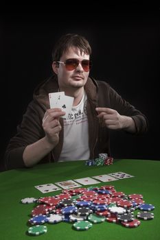 Man with sun glasses playing poker on green table. Chips and cards on the table.