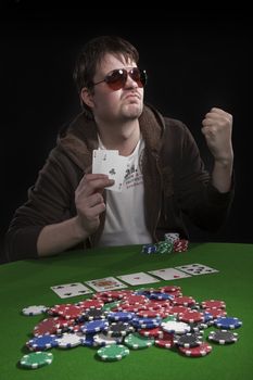 Man with sun glasses playing poker on green table. Chips and cards on the table.