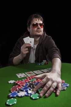 Man with sun glasses playing poker on green table. Chips and cards on the table.