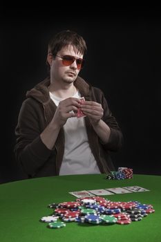 Man with sun glasses playing poker on green table. Chips and cards on the table.