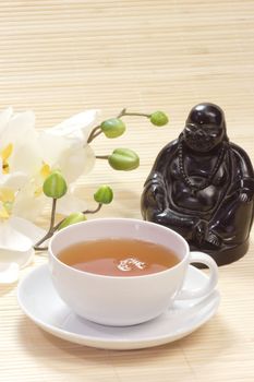 Green tea in a teacup with buddha figure and white blossoms