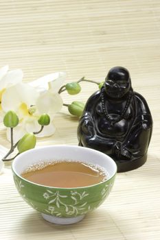 Green tea in a mug with buddha figure and white blossoms