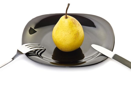 Fresh yellow pear on a black plate with fork and knife