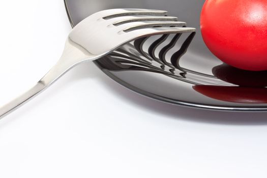 Red tomato on a black high-gloss plate with stainless fork 
