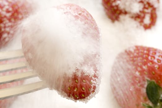 Granulated sugar being poured over ripe strawberries