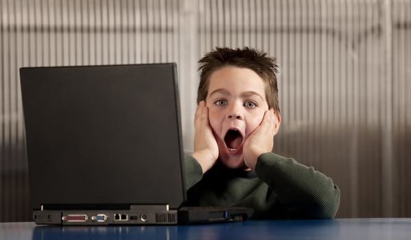 Shocked young boy reacting to info on a laptop computer