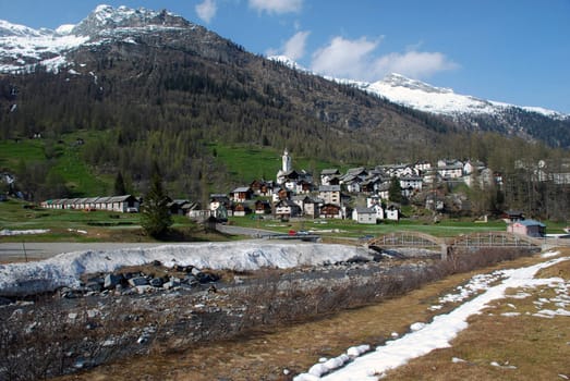 Bosco Gurin retains the charm of one of the most charming mountain villages of Switzerland, seen from Rovana river. The picturesque town, founded in 1253 by settlers Walser actually looks beautiful and intact with its distinctive stone houses and wood, animl farm at left, bridge at right, Alps at background, springtime 