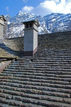 Havy Stone roof and the chimnay of traditional house in Bosco Gurin,  one of the most charming mountain villages of Switzerland. There are Alp mountains and the sky at the background