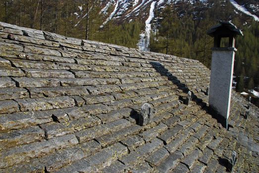 Havy Stone roof and the chimnay of traditional hous in Bosco Gurin. There is mountains forest in springtime  at the background