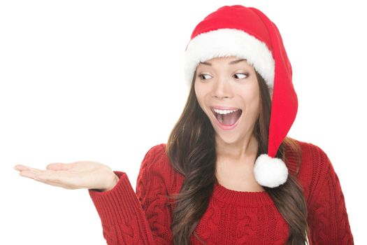 Christmas woman copy space. Excited santa girl presenting your product looking sideways on copyspace with open hand palm. Closeup of mixed Asian Caucasian female model isolated on white background. Less excited smiling version also available in portfolio.