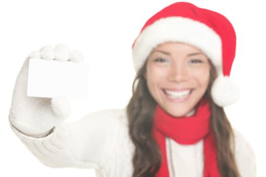 Christmas woman showing business card / blank white sign with copy space. Young woman smiling in Santa hat, sweater and gloves. Isolated on white background. Mixed asian / caucasian female model. Focus on blank sign card. 