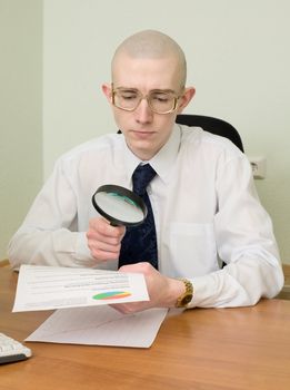 The boss with a magnifier in a hand on a workplace