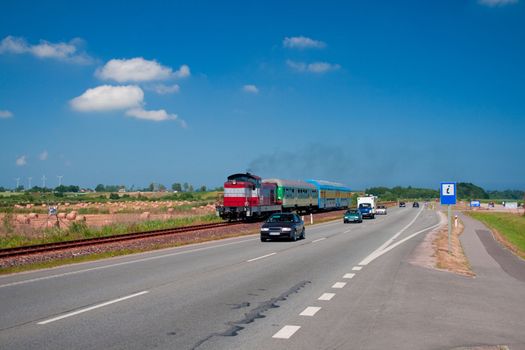 Landscape with a passenger train and road with moving cars
