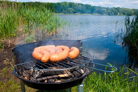 Fresh sausage preparing on grill at the lakeshore
