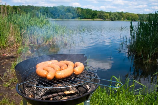 Fresh sausage preparing on grill at the lakeshore
