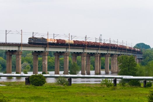Fuel freight train passing the steel bridge over the river
