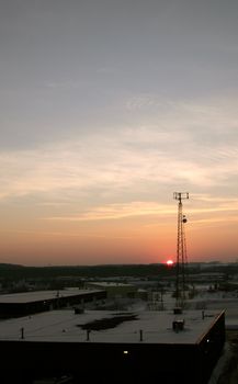 The silhouette of a cell phone tower shot against the orange cast of the setting sun.
