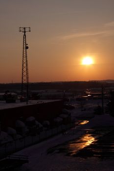 The silhouette of a cell phone tower shot against the orange cast of the setting sun.
