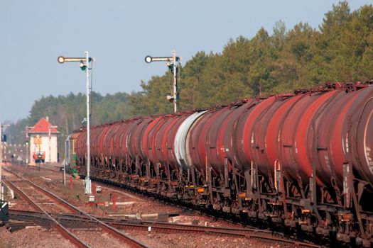 Freight train with fuel passing the station in the middle of the woods
