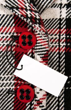Blank label or price tag attached to a button of a stylish red checked coat.