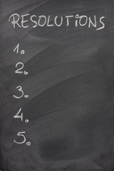 blank list of five resolutions handwritten with white chalk on a blackboard with strong eraser patterns
