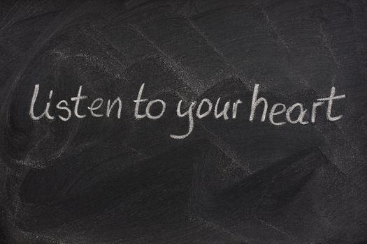 listen to your heart phrase handwritten with white chalk on a blackboard with eraser smudge patterns