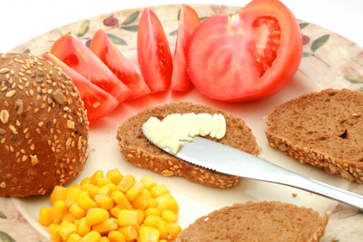 Whole-meal roll with butter, corn and tomato on the plate