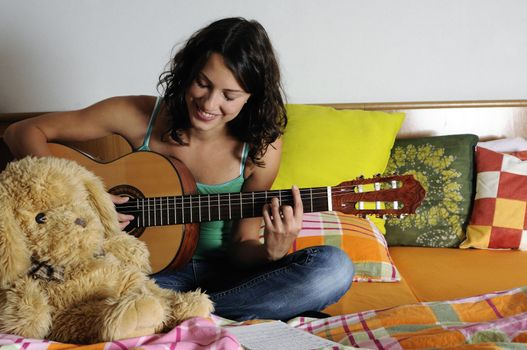 Beautiful teen girl playing guitar in her bedroom