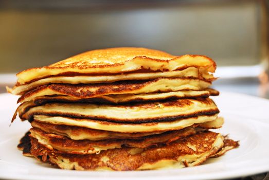 Close up of a pile of pancakes served on a white plate.