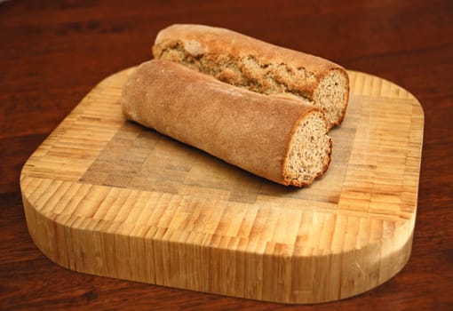 Homemade rye caraway bread cut in half on a wooden cutting board on a table.