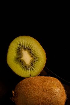 Whole and halved kiwi on black background