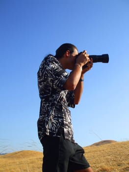 Young man photographer holding a photo camera outdoors.