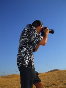 Young man photographer holding a photo camera outdoors.