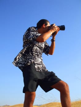 Young man photographer holding a photo camera outdoors.