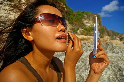 Asian woman on the beach, applying make-up, Dreamland, Bali, Indonesia.