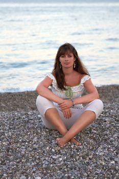 Calm, young woman sitting on the pebble sea beach
