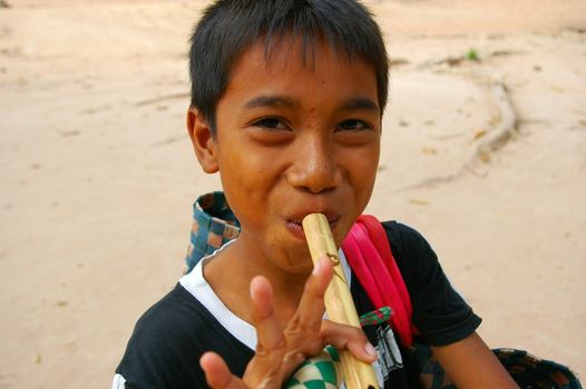 Cambodian boy playing one of the flutes he is trying to sell, Bayon Temple, Siem Reap, Cambodia.