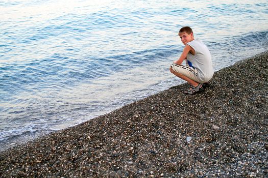 Smiling boy sitting at the evening pebble beach