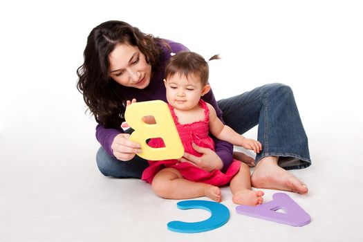 Mother, nanny, or teacher teaching happy baby to learn alphabet, A, B, C, with letters in a playful way, while sitting on floor.