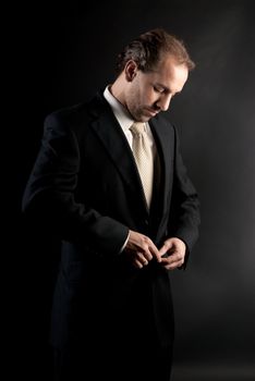 businessman buttoning jacket, getting dressed, on dark background