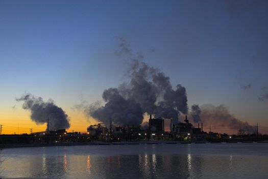 Factory over the river with smoke coming out of the chimneys